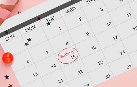 Calendar with marked Birthday date flat lying on pink background with party confetti, creative...