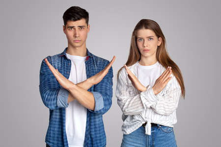 Upset millennial couple of student friends in casual, crossed their arms and look at camera, isolated on gray background, studio shot, empty spaceの写真素材