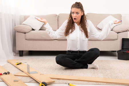 Furniture Installation. Shocked Woman Having Trouble Assembling Wooden Shelf Herself Using...