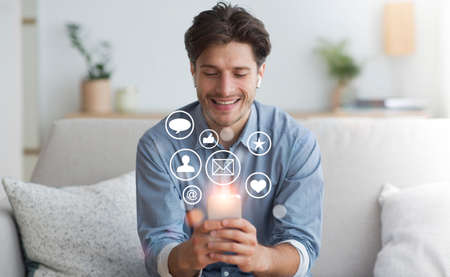 Cheerful Guy Using Mobile Phone Browsing Internet, Networking And Texting In Social Media Sitting On...