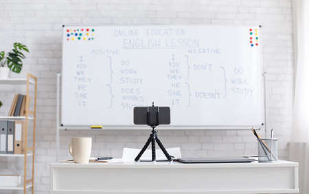 Workplace for blogger, tutor or English teacher. Board with rules near white brick wall, smartphone...