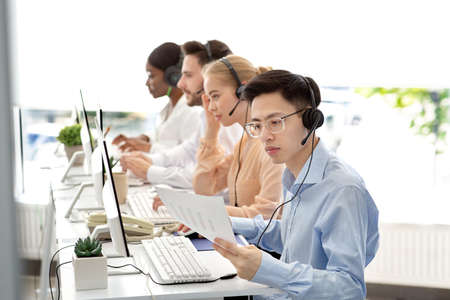 Asian hotline operator working with documents, providing technical support services to clients, free space. Call centre representatives talking to customers or selling goods onlineの写真素材