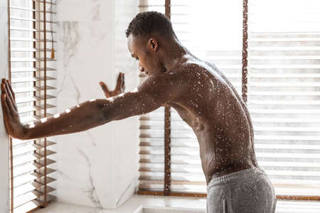 African Guy Enjoying Shower Standing Under Steaming Hot Water Washing Body And Relaxing In Modern Bathroom At Home. Bodycare And Everyday Hygiene For Men Concept.の写真素材