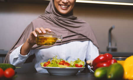 Muslim Woman Cooking In Kitchen, Making Vegetable Salad With Oil Dressing At Home, Wearing Hijab Headscarf. Arabic Wife Preparing Healthy Dinner Working Indoor. Arab Cuisine, Recipes. Croppedの写真素材