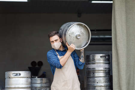 Young man working at warehouse in brewery or employee with keg. Handsome millennial man with tattoos...