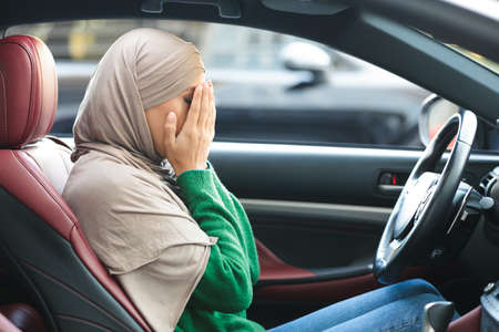 Stressed muslim female driver sitting in car, covering face with hands, having accident, failed...