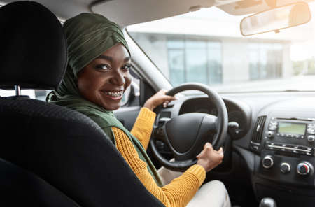 Buying Automobile. Smiling Black Muslim Lady In Hijab Testing New Car, Sitting On Front Seat...