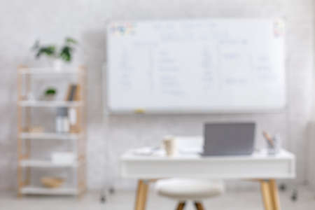 Blurred photo of minimalist living room interior at home for work and hobby. Blackboard on white brick wall, laptop, cup, notepad and pencils on table with chair, flat lay, free space, nobodyの写真素材