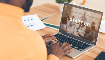Black entrepreneur using online START UP YOUR BUSINESS platform on his laptop, panorama. Managing new project remotely, creating brand website, digital promotion conceptの写真素材