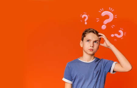 Thoughtful Caucasian teenager searching for creative solution to problem on orange background,...