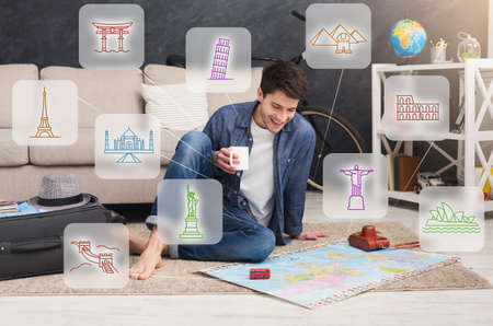 Planning Vacation. Traveler Guy Looking At World Map Choosing Travel Destination Sitting On Floor...