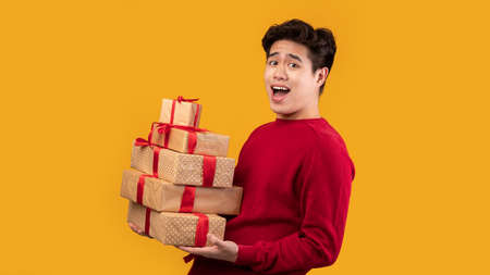 Buying Holiday Gifts. Portrait of half-turned excited asian man carrying pile of present boxes with...