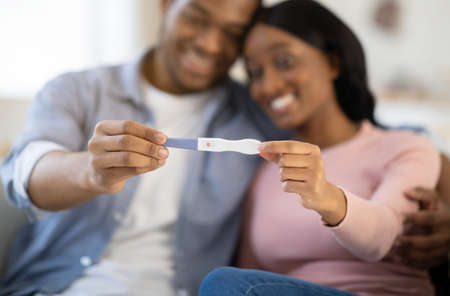 Young balck couple showing positive pregnancy test at home, selective focus on hands. Happy future parents expecting child, excited over good news. Parenthood and childbearing conceptの写真素材