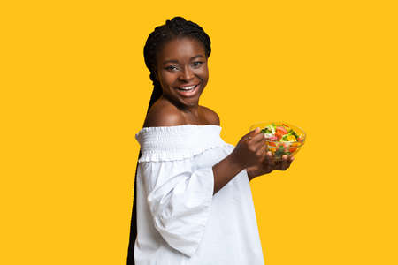 Joyful Black Lady Eating Vegetable Salad From Bowl And Looking At Camera, Enjoying Heathy Nutrition...
