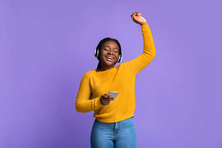 Listen Music Online. Carefree Black Woman With Wireless Headphones And Smartphone Dancing With...