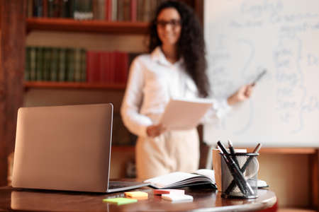 Workspace. Selective focus on laptop on the table, smiling woman in eyeglasses standing at...