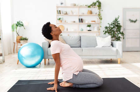 Side view of black pregnant woman doing backbend during meditation or yoga at home. Beautiful...