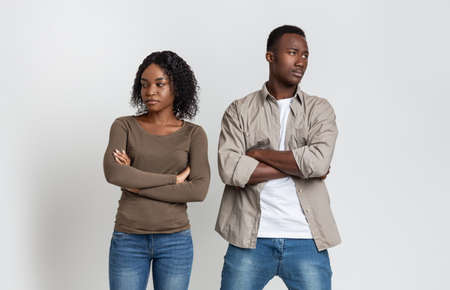 Break up, troubles, misunderstanding in relationships or marriage. Upset african-american man and woman standing next to each other with arms crossed after fight, gray studio backgroundの写真素材