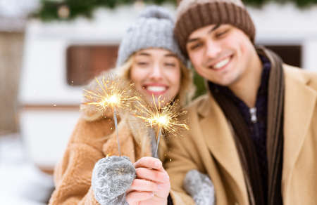 Festive Mood. Cheerful Young Couple Posing With Sparklers Outdoors At Winter Day, Celebrating Christmas Holidays Together, Having Fun At Camping, Standing Near Motorhome Campervan, Selective Focusの写真素材