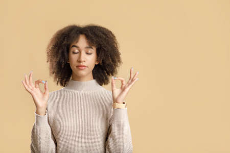 Meditate, wellness and be calm. Cheerful curly young african american female with closed eyes practicing yoga and breathing, isolated on yellow background, cut out, studio shot, empty spaceの写真素材