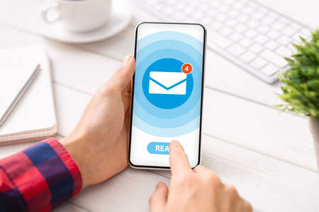 Businessman reading incoming messages from email app on smartphone at office desk, creative collage. Cropped view. Modern communications and online marketing conceptの写真素材