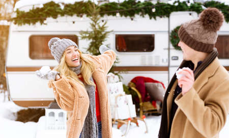 Winter Pastime. Young Cheerful Couple Having Fun Together Outdoors At Campsite, Throwing Snowballs At Each Other And Laughing, Playful Man And Woman Enjoying Christmas Holidays And Cold Weatherの写真素材