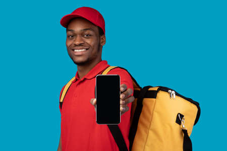 Application For Online Order. Smiling black deliveryman showing mobile phone with blank screen for...