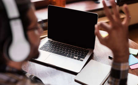Video Call. Indian Student Guy At Laptop Gesturing Okay To Empty Computer Screen Sitting At Desk Indoor, Wearing Headphones. Distance Learning, Online Education Concept. Mockup, Back Viewの写真素材