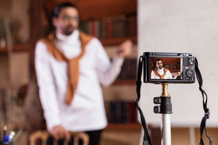 Teacher Blogger Guy Making Video Lesson For Educational Blog Standing Near Blackboard Indoor, Focus On Camera. E-Teaching And Online Learning, Knowledge And Modern Distance Education. Shallow Depthの写真素材