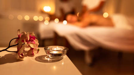 Spa Composition With Aromatic Candle And Exotic Orchid Flowers. Unrecognizable Couple Receiving Relaxing Massage At Spa. Beauty, Wellness And Relaxation. Selective Focus, Panorama With Copy Spaceの写真素材