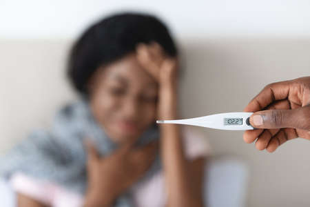 Cold, flue, coronavirus concept. Black woman suffering from fever, selective focus on thermometer in...