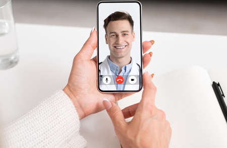 Sick Lady Talking With Male Doctor Online Via Video Call On Mobile Phone During Virtual Medical Consultation Sitting Indoors. Female Patient Chatting With Physician By Smartphone. POV, Croppedの写真素材