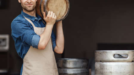 Loading of products for beer fermentation and small business. Strong millennial worker guy in apron...