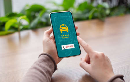 Unrecognizable woman using app on smartphone for online taxi ordering, browsing modern application for transportration booking, sitting at table outdoors, creative collageの写真素材
