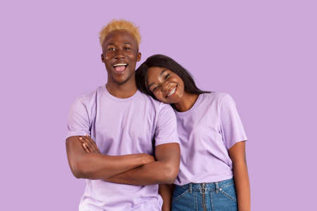 Cheerful black woman putting head on her boyfriends shoulder, expressing affection on lilac studio background. Romantic African American couple posing and smilingの写真素材
