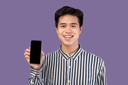 I Recommend This Website. Smiling young asian man holding smartphone with black empty screen in...