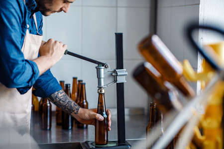 Drink production, employee works on beer manufacturing, craft plant. Young serious worker in apron...