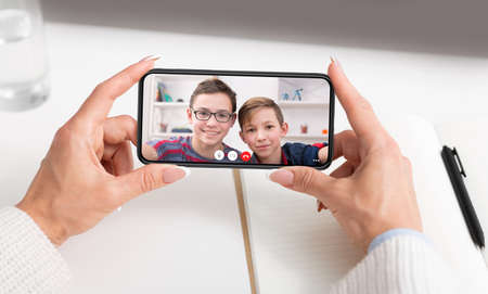 Unrecognizable woman having videocall with her sons while working at office, using mobile...