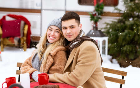 Loving young couple having romantic date in camping, enjoying winter picnic, sitting at table and...