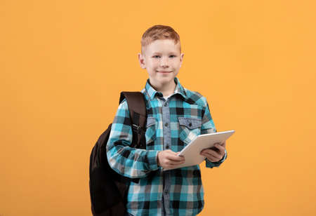 Technologies in school education. Smiling smart schoolboy with backpack holding digital tablet over...