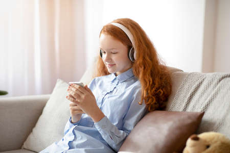 Everyday Life Concept. Calm Red-Haired Schoolgirl Relaxing On The Couch At Home, Listening To Music...