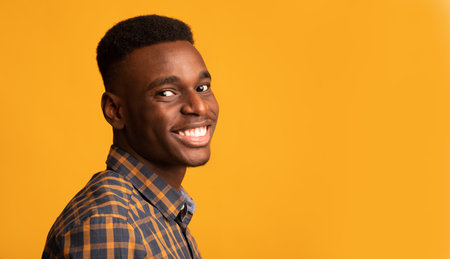 Portrait Of Young African American Guy Smiling To Camera Standing Half-Turned In Studio, Cheerful...