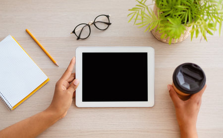 Modern Technology Concept. Top above high angle view of african american woman using digital tablet with empty black blank screen for template mock up, sitting at desk, drinking coffee, copy spaceの写真素材
