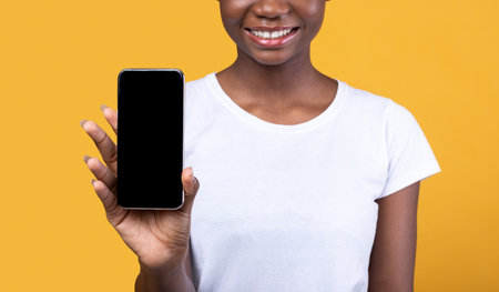 Unrecognizable Black Woman Showing Mobile Phone Empty Screen To Camera Recommending Application For Smartphone Posing Over Yellow Background In Studio. Cropped, Mockupの写真素材