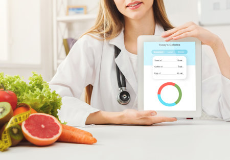 Doctor dietologist holding digital tablet with opened app for daily calories counting, siiting at desk with fruits and vegetables, creative collage for healthy eating, dieting, and weight loss conceptの写真素材