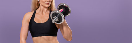 Sportswoman bodybuilder coach and online workout for blog. Serious adult muscular lady in sports bra with wireless headphones doing exercise with dumbbells, isolated on purple background, panoramaの写真素材