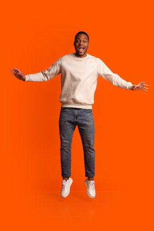 Excited Black Guy Jumping In Air Over Orange Background, Having Fun In Studio, Portrait Of Positive...