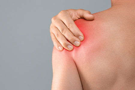 Closeup of topless man suffering from shoulder pain injury, rubbing sore zone over grey studio background, copy space, cropped. Healthcare and medical concept, sports traumatology and orthopedicsの写真素材
