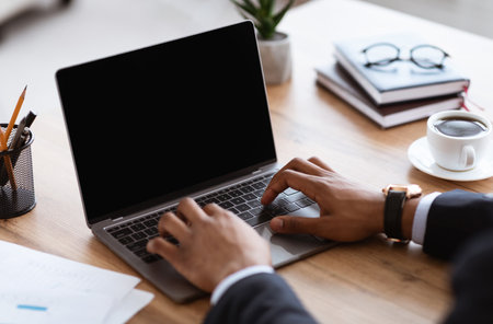 Closeup of african american businessman hands typing on small modern laptop with blank screen, black manager working online in his office, having online conference or video call with partners, mockupの写真素材