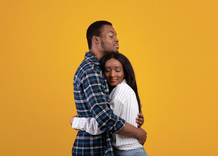 Romantic relationship in couple, love, positive emotional and happiness. Young happy african american husband and wife in casual hugging, isolated on yellow background, empty space, studio shotの写真素材